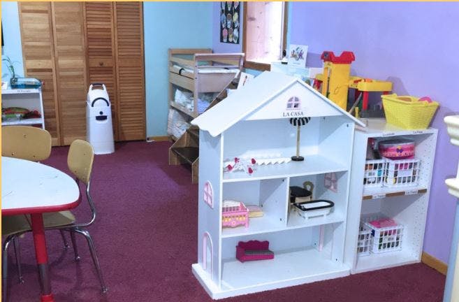 Playroom with a dollhouse, small table and chairs, and storage shelves