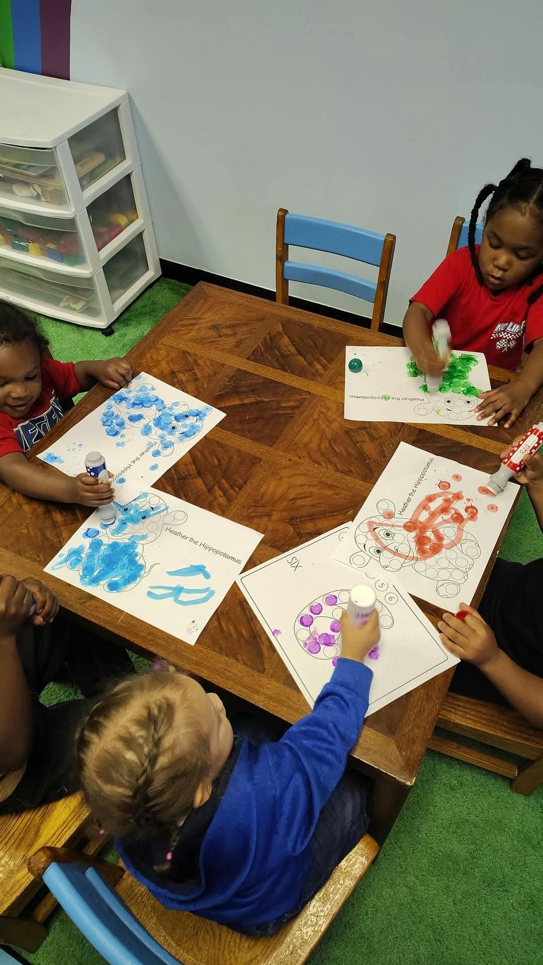 Children sitting at a table coloring with dot markers