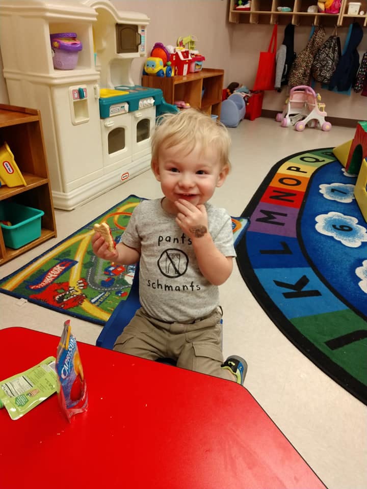 Child sitting at a red table in a classroom, holding food