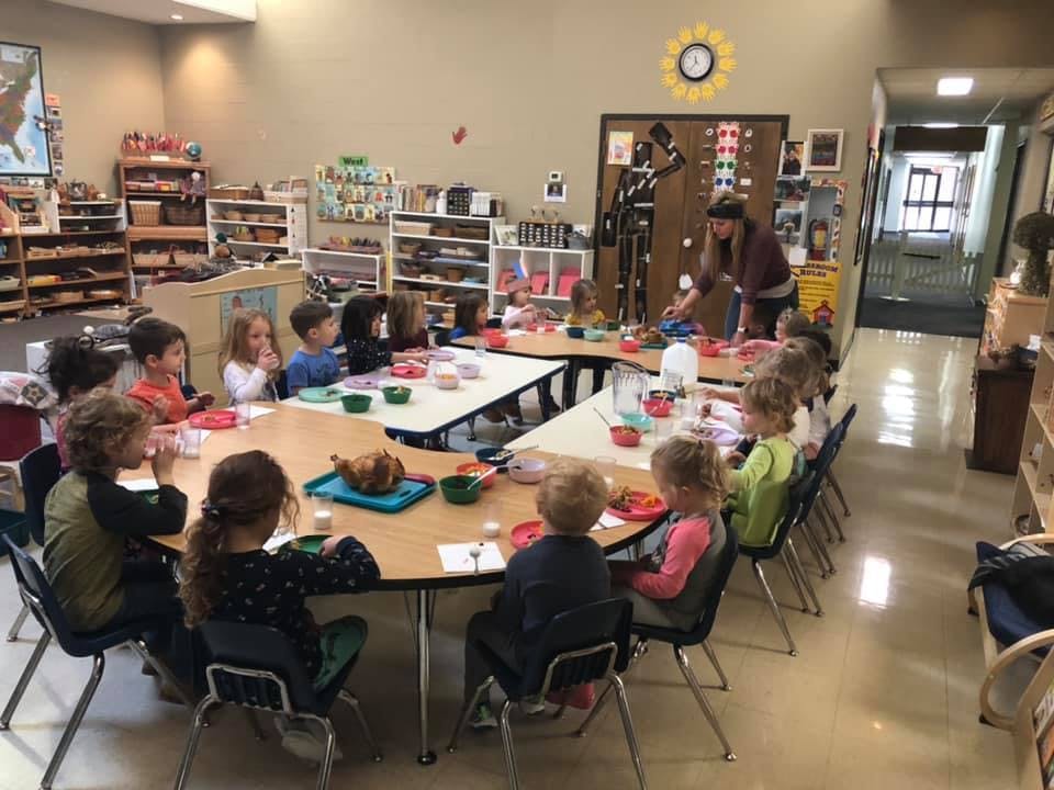 Children sitting at tables in a classroom with an adult