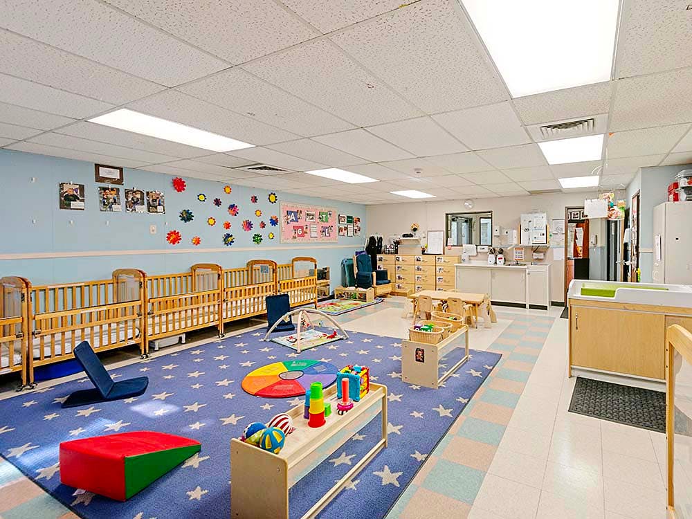 cribs in a daycare room with a star-patterned rug and toys