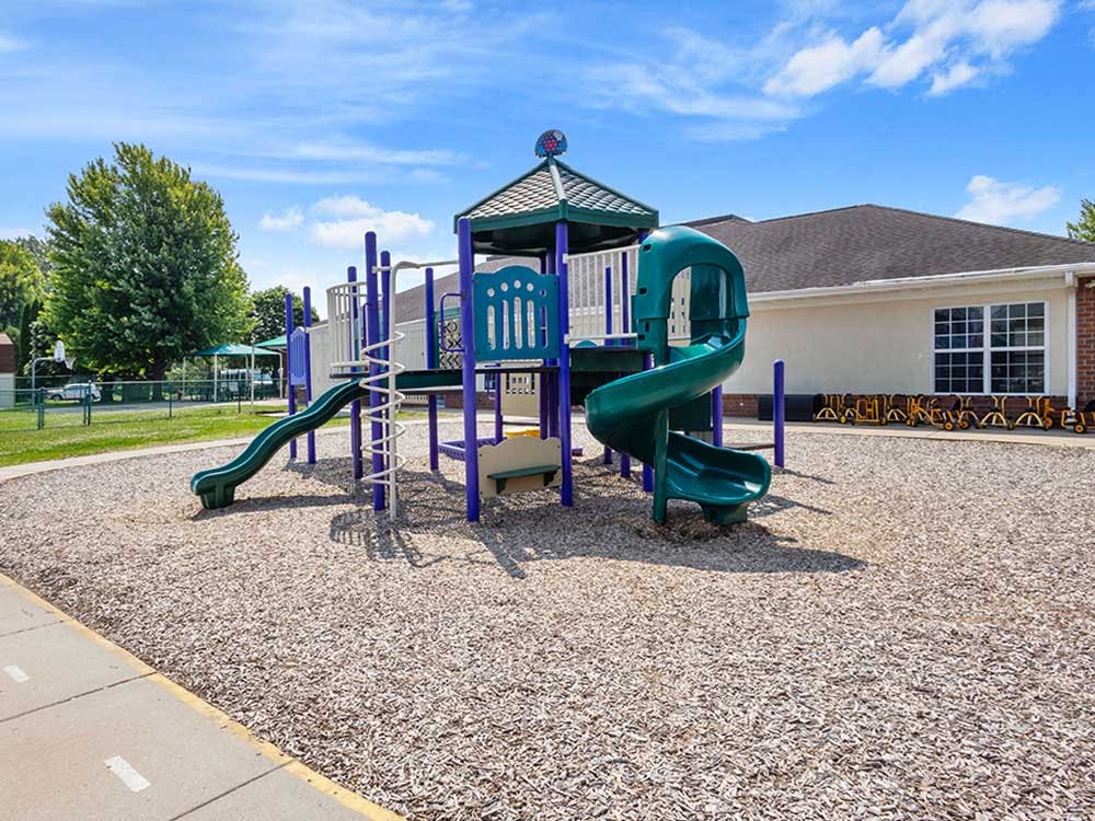 Playground with green and purple slides, structure, and wood chip ground