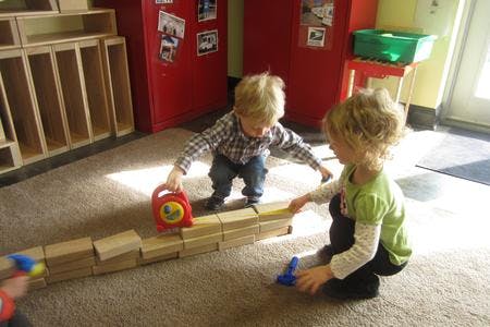 Two children playing with wooden blocks on a carpeted floor