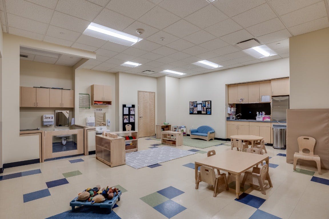 Empty classroom with small tables and chairs, play kitchen, and blue and green floor tiles