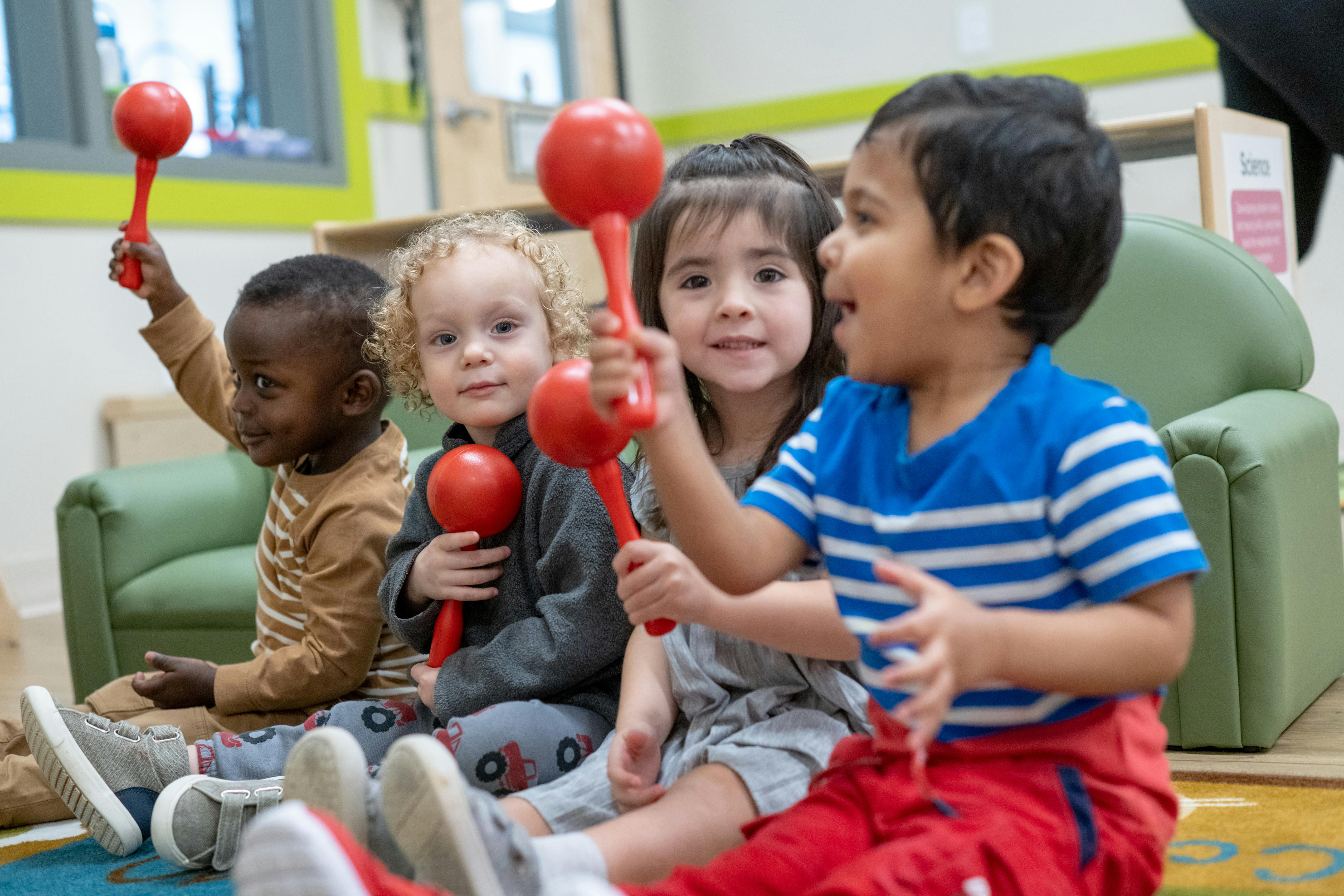 Four children sitting on the floor playing with red maracas