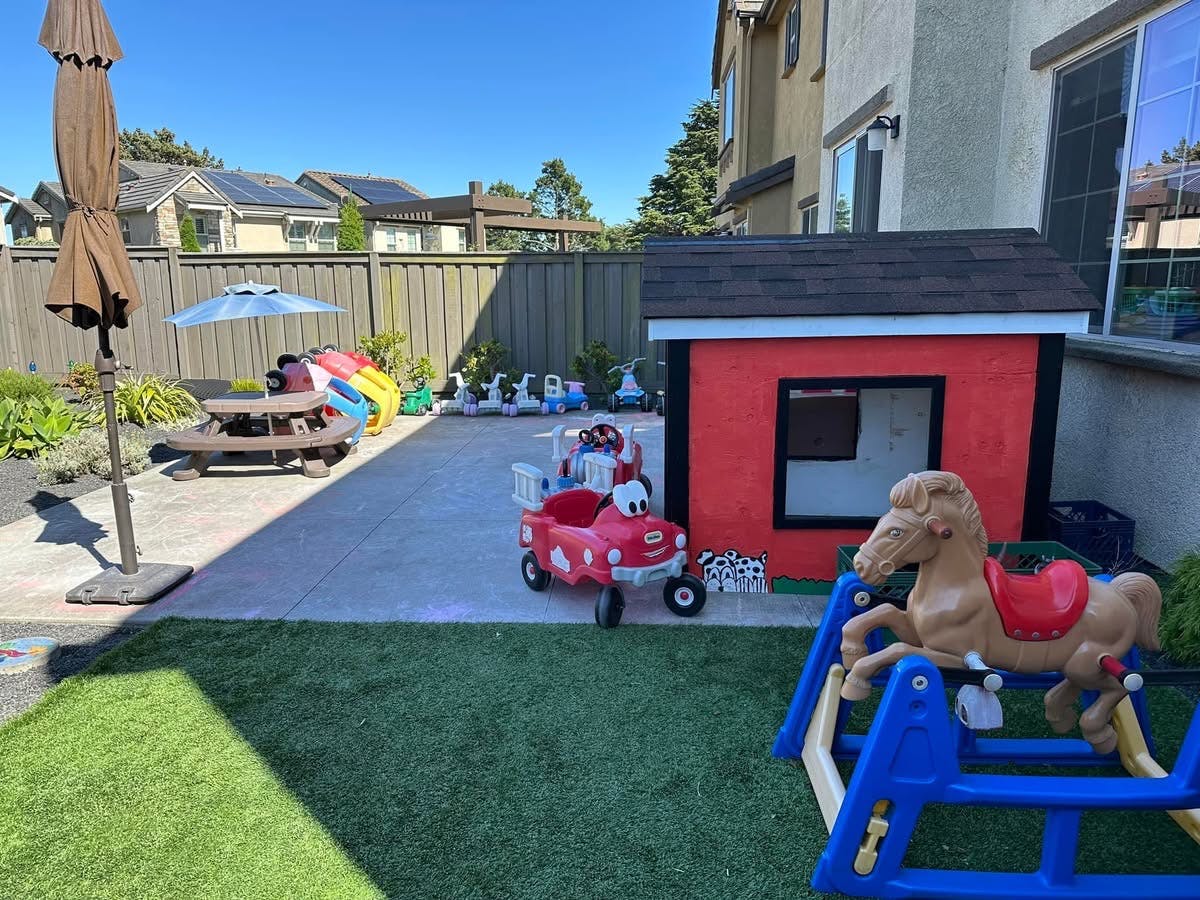 Backyard play area with a red playhouse, toy car, and rocking horse