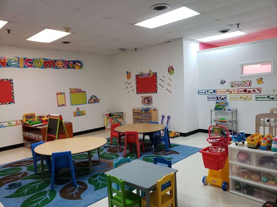 Empty classroom with small tables and chairs, colorful rug, and wall decorations