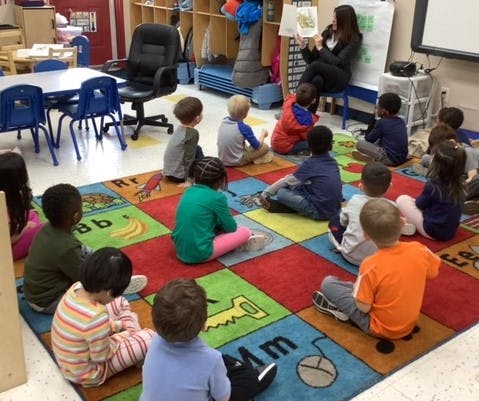 Adult reading a book to a group of children in a classroom