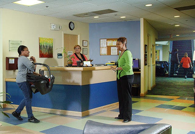 Person carrying infant car seat approaching a reception desk