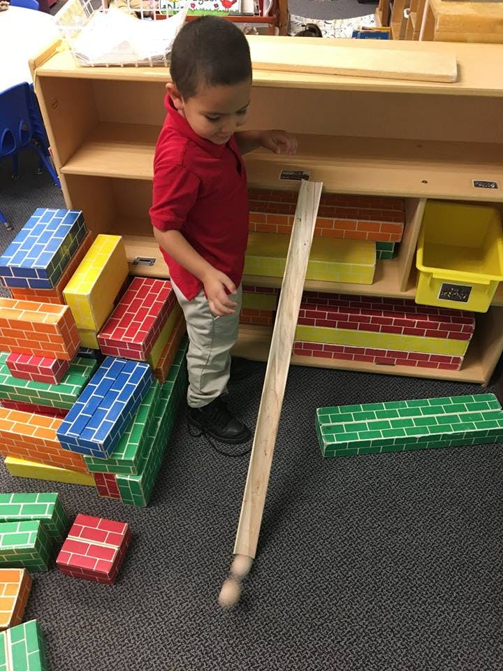 Child standing next to a wooden ramp and colorful blocks in a classroom