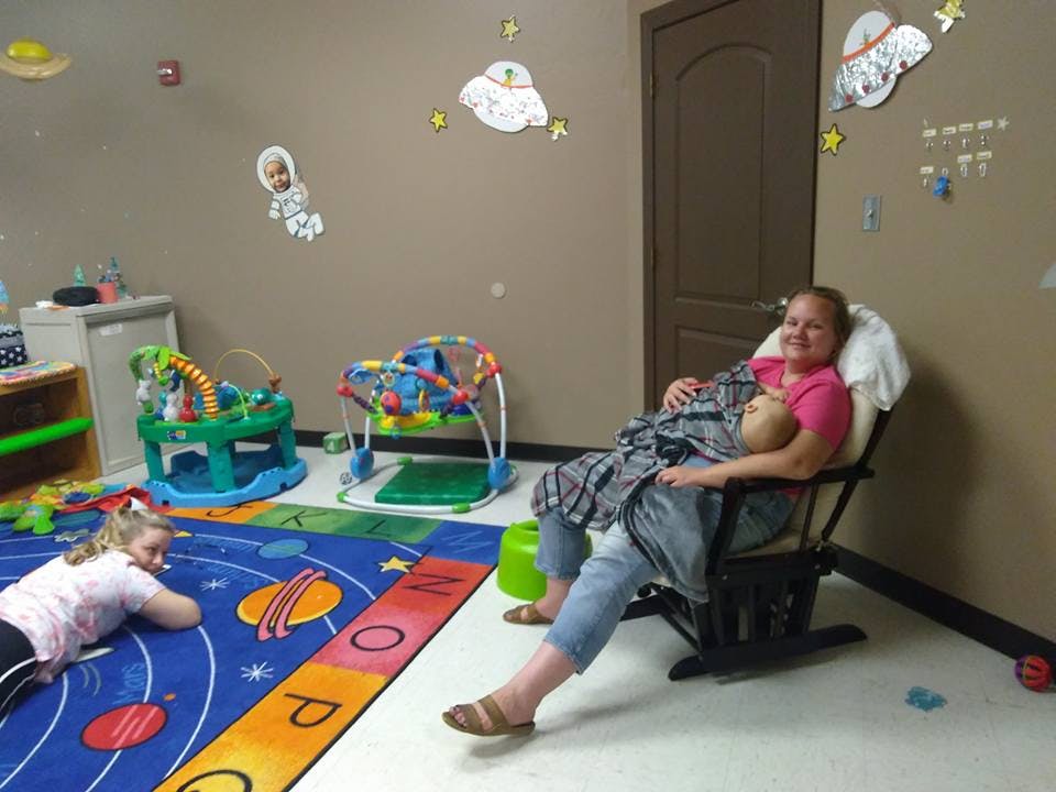 Person sitting in a rocking chair holding a baby, child lying on a rug