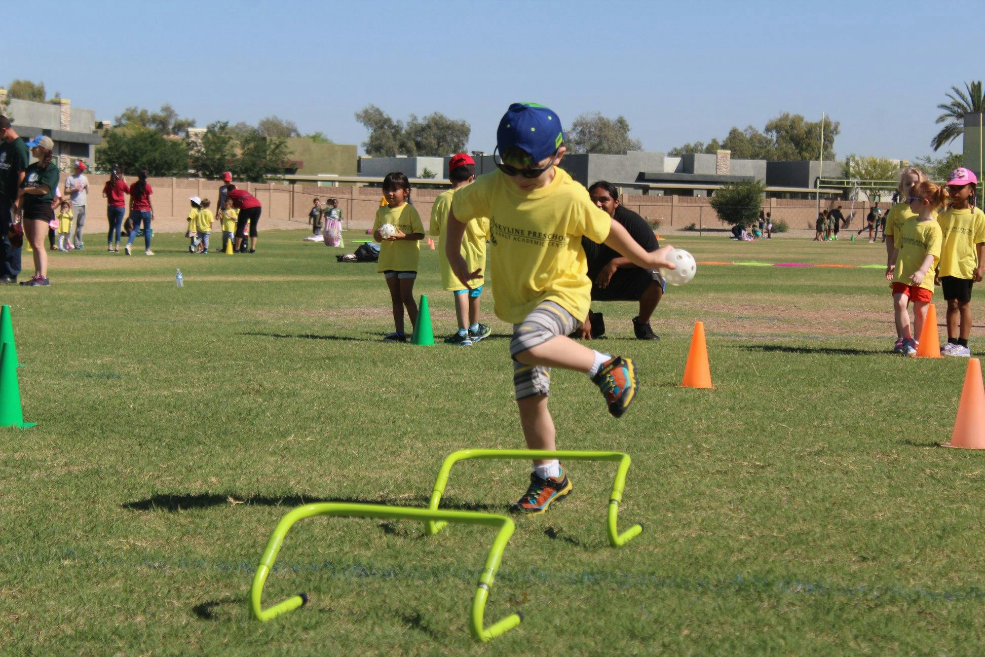 Child in yellow shirt stepping over a hurdle on a grassy field