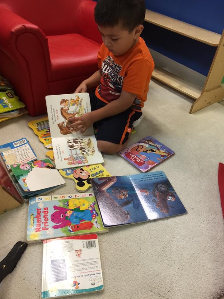 Child sitting on floor looking at an open book surrounded by other books