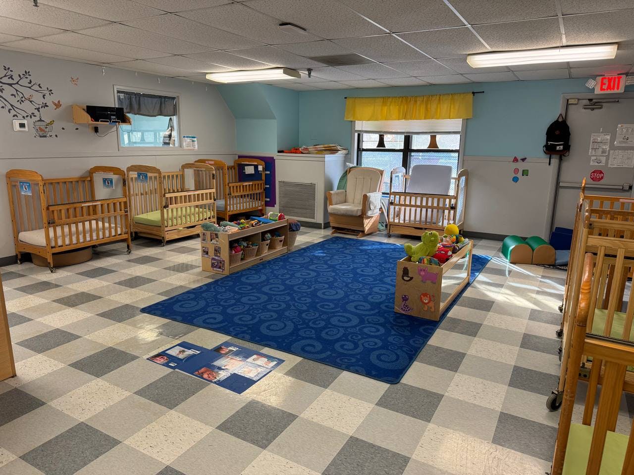 A room with several cribs, a blue rug, and toys