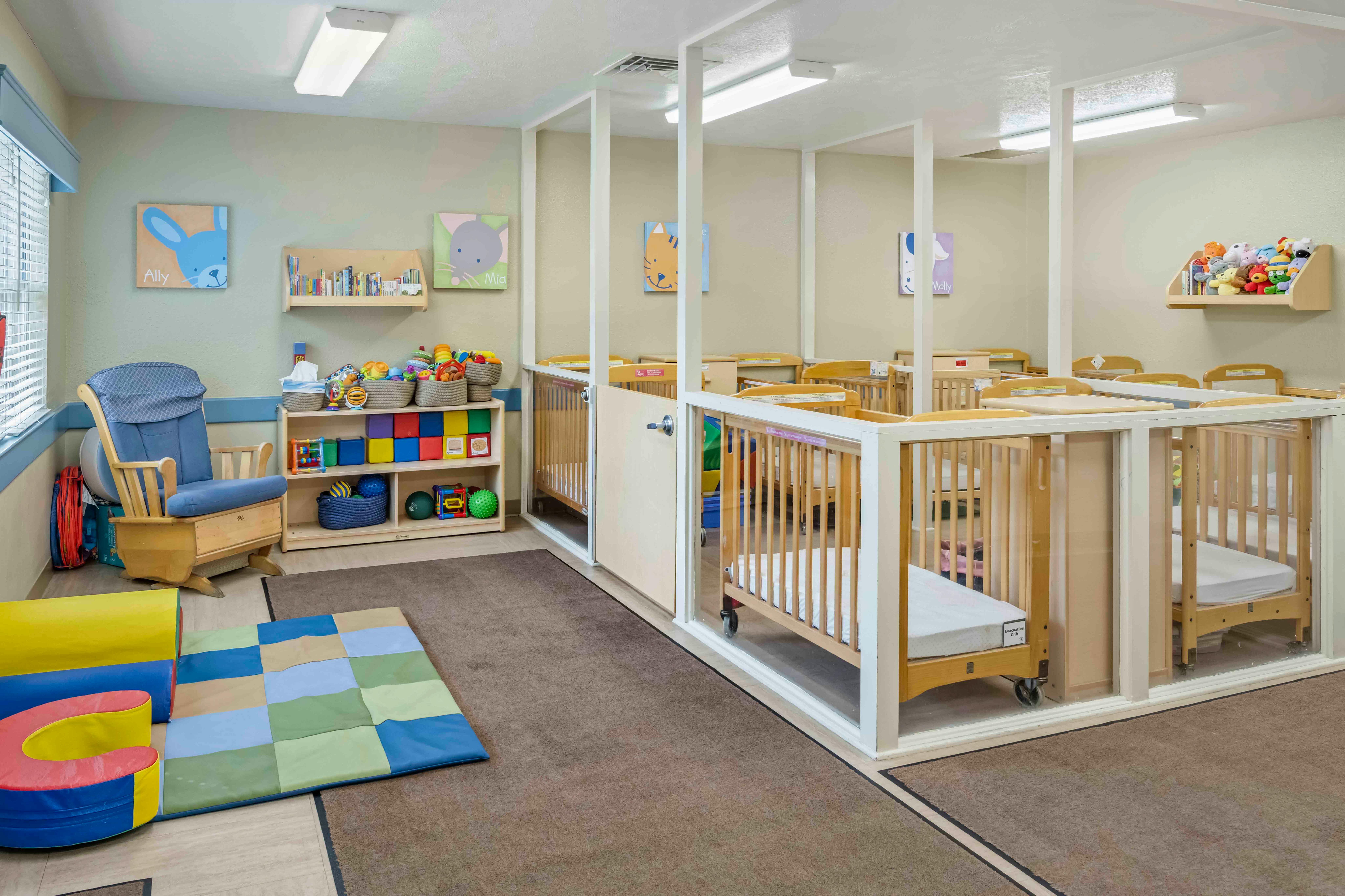 A room with multiple cribs, a rocking chair, shelves, and play mats