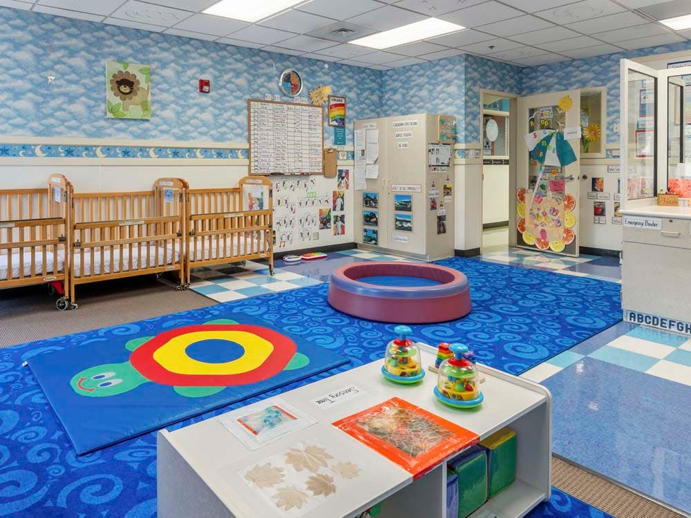 Classroom with cribs, play mat, and toddler toys
