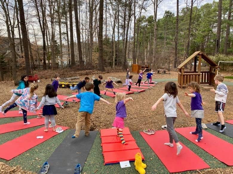 Children doing yoga poses outdoors on red mats