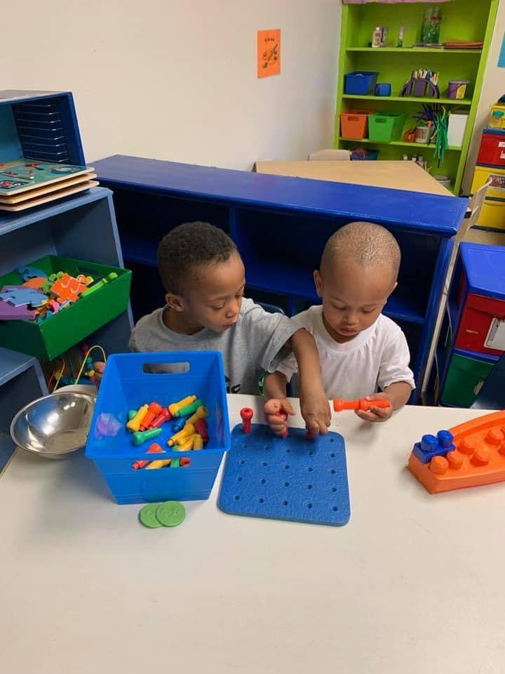 Two children playing with toys at a table in a classroom