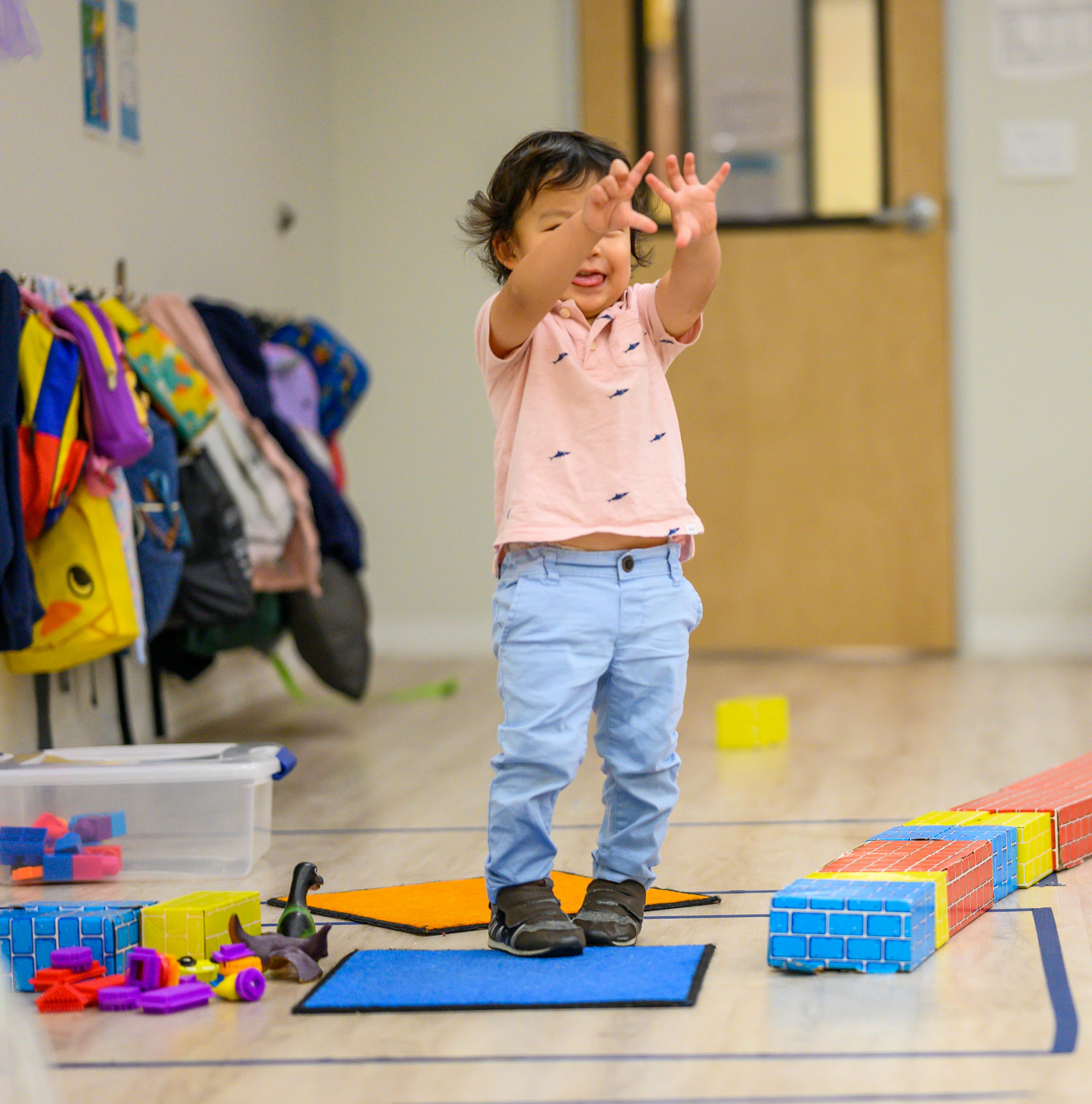 Child standing with hands raised in a classroom