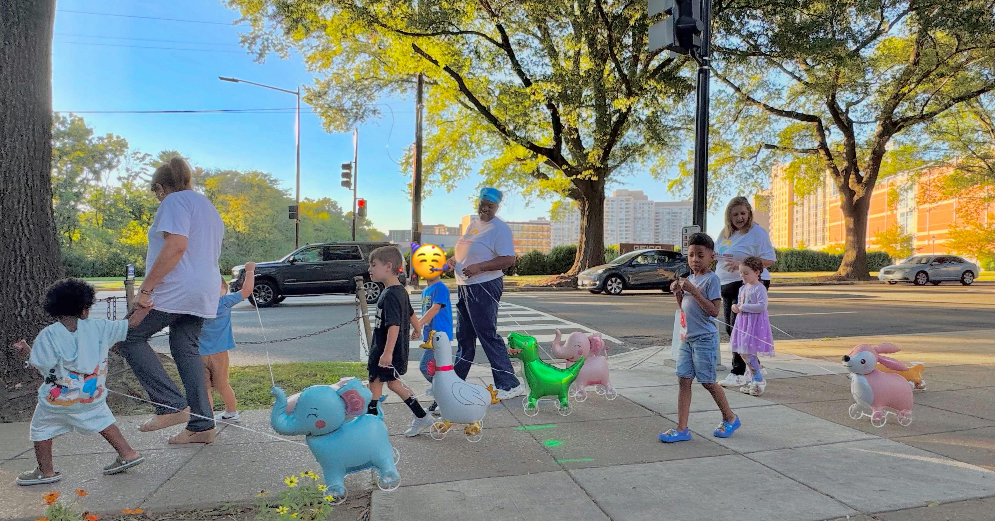 People and children walking on a sidewalk with animal balloons
