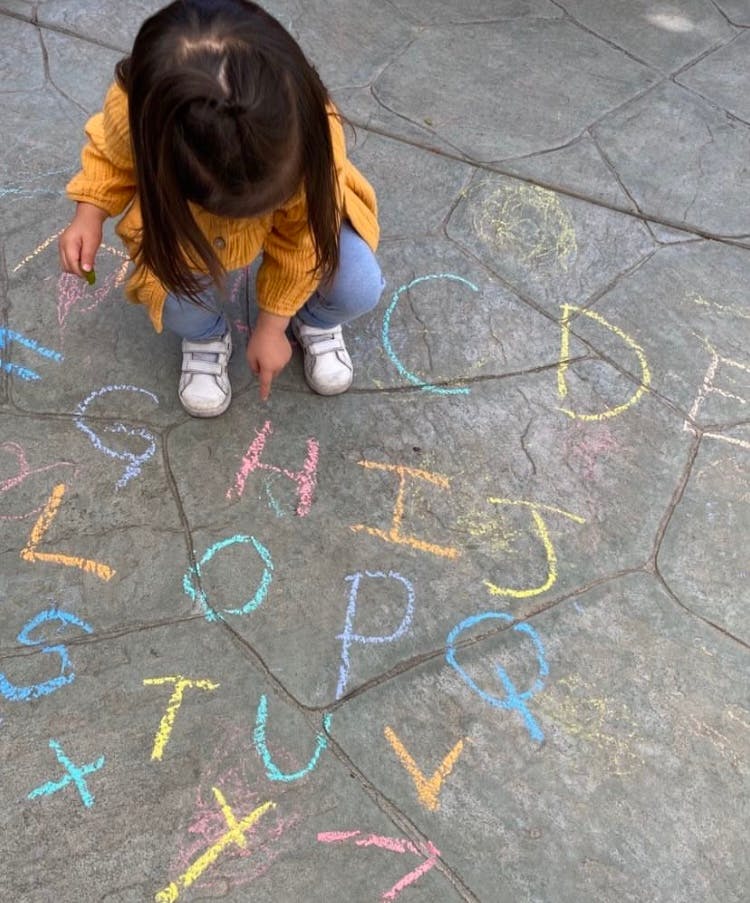 Child pointing at chalk letters on the ground