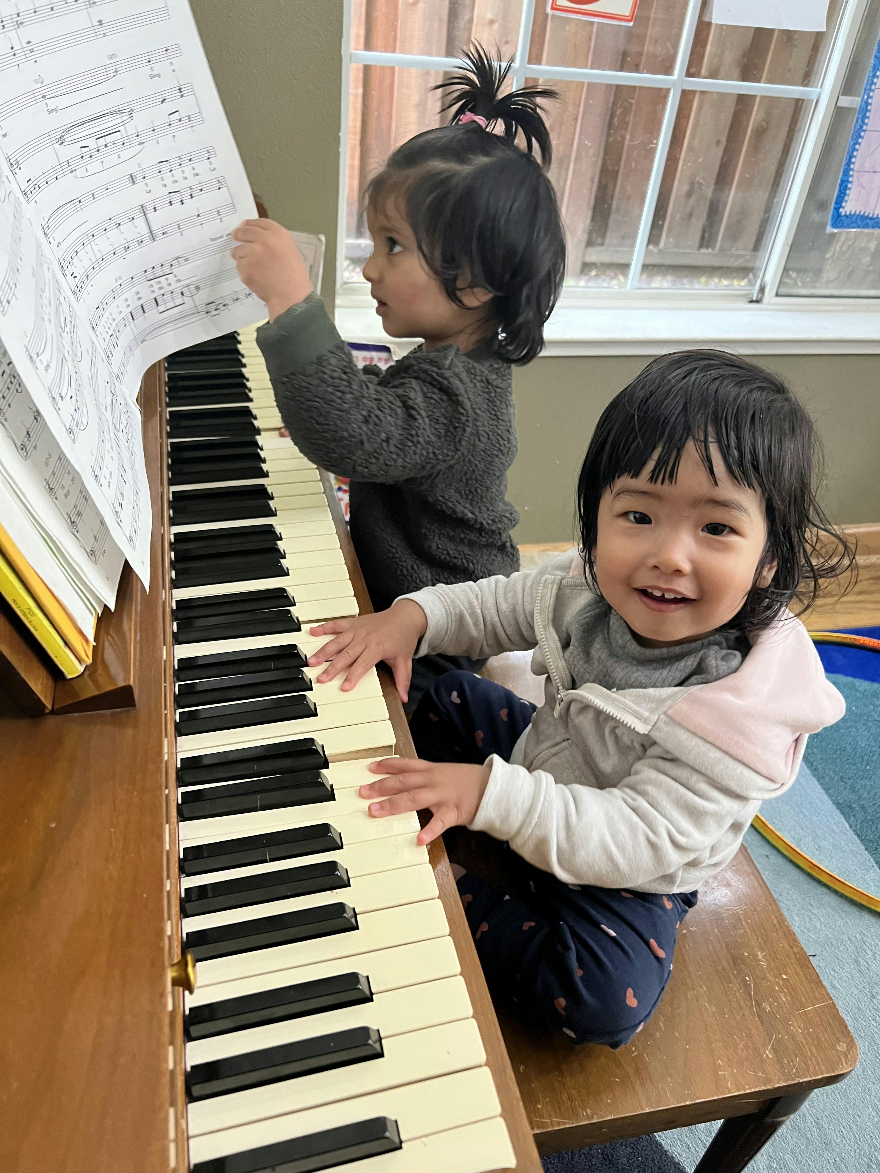 Two children at a piano, one reading sheet music and the other playing keys