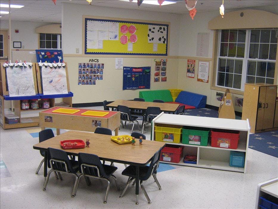An empty early childhood classroom with small tables and chairs