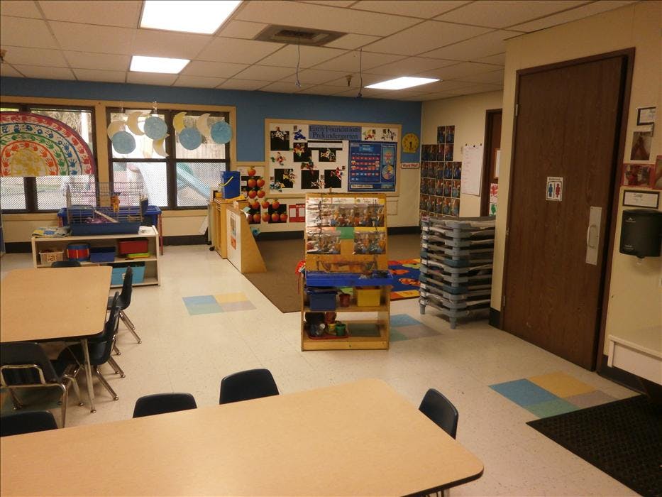 An empty classroom with tables, chairs, and classroom decorations