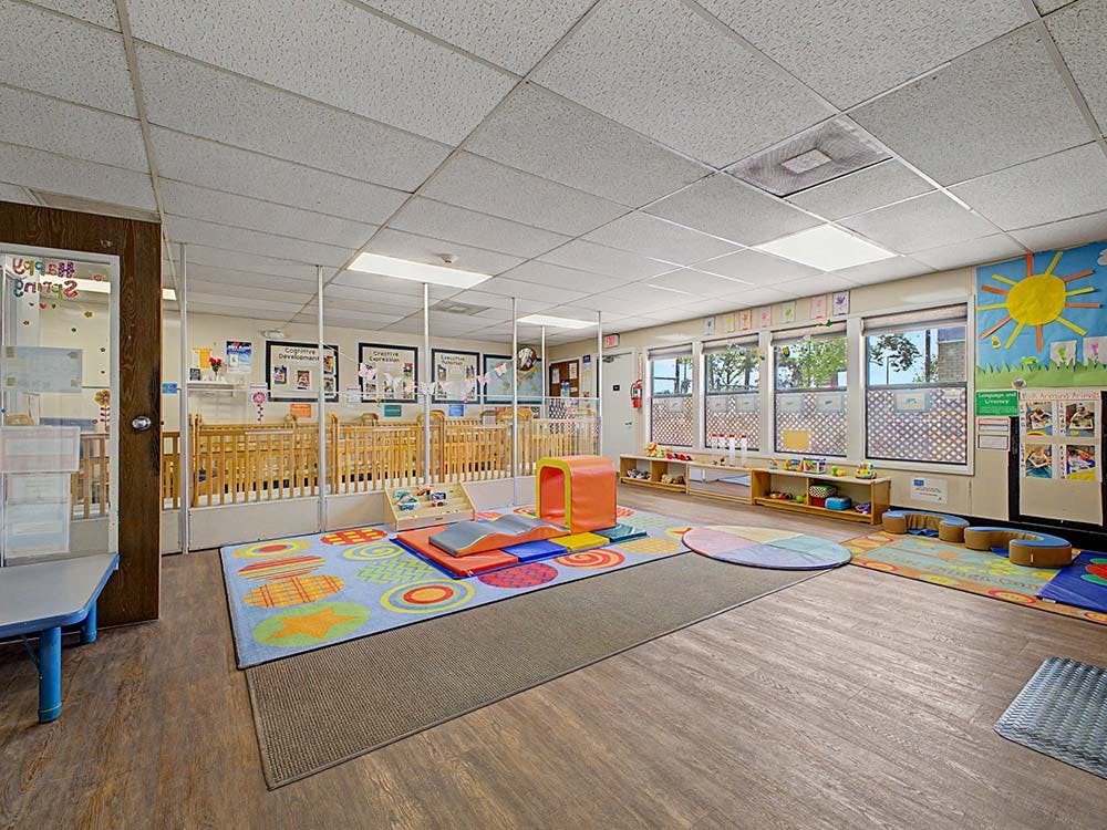 Daycare room with cribs, play mats, and learning charts on the walls