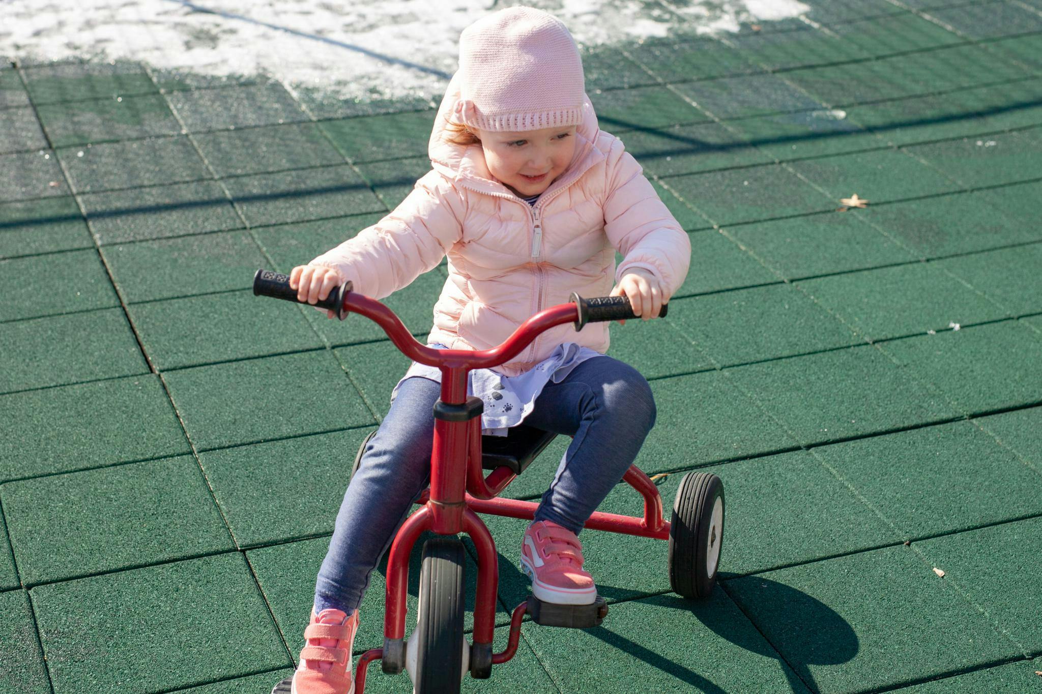 Child riding a red tricycle on a green tiled surface