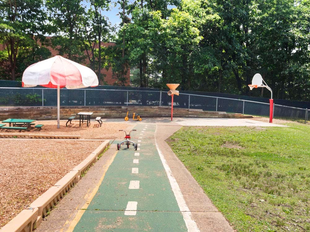 tricycle and other toys on a playground with a basketball hoop and umbrella