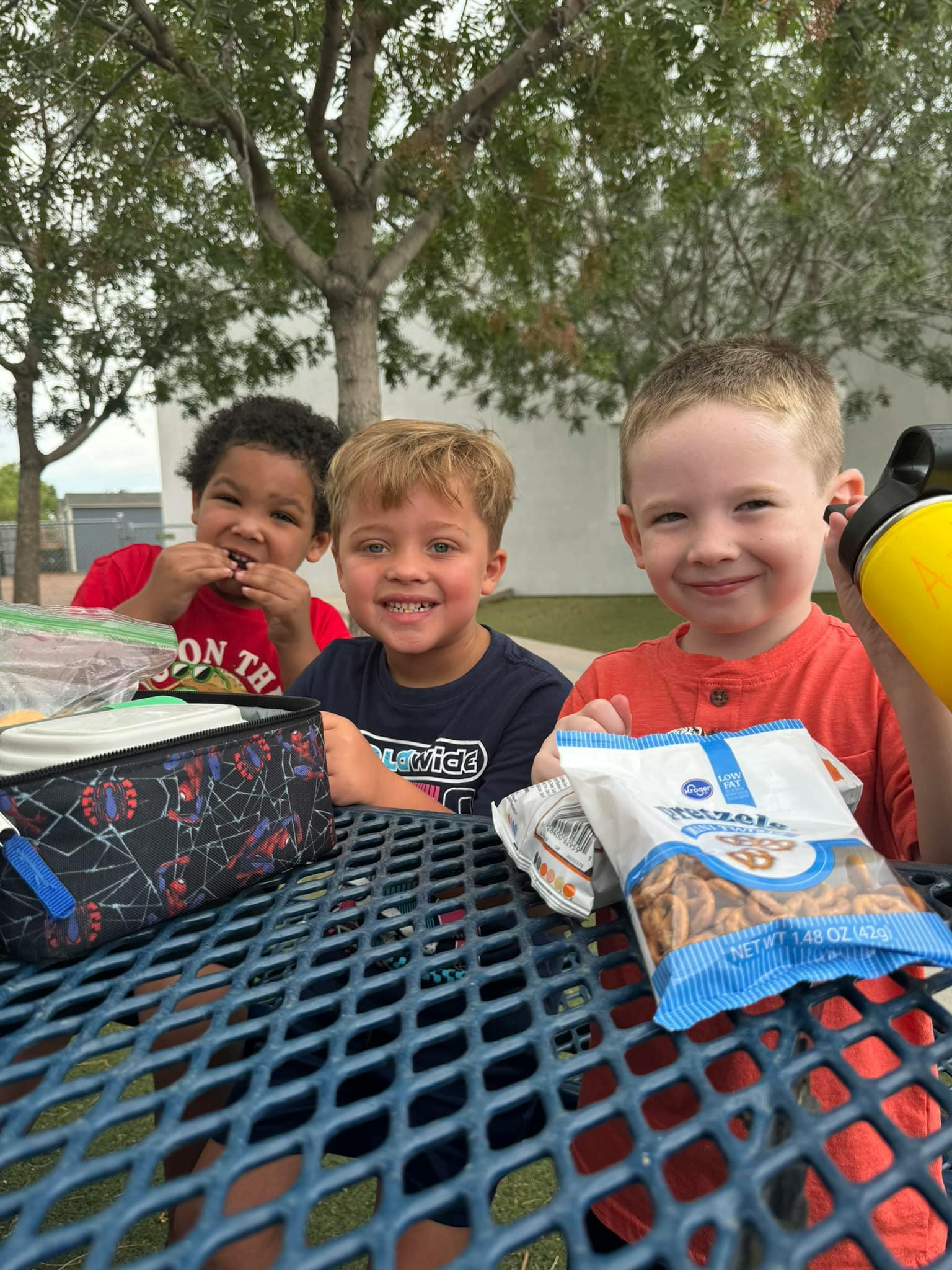 Three children sitting at a picnic table with snacks