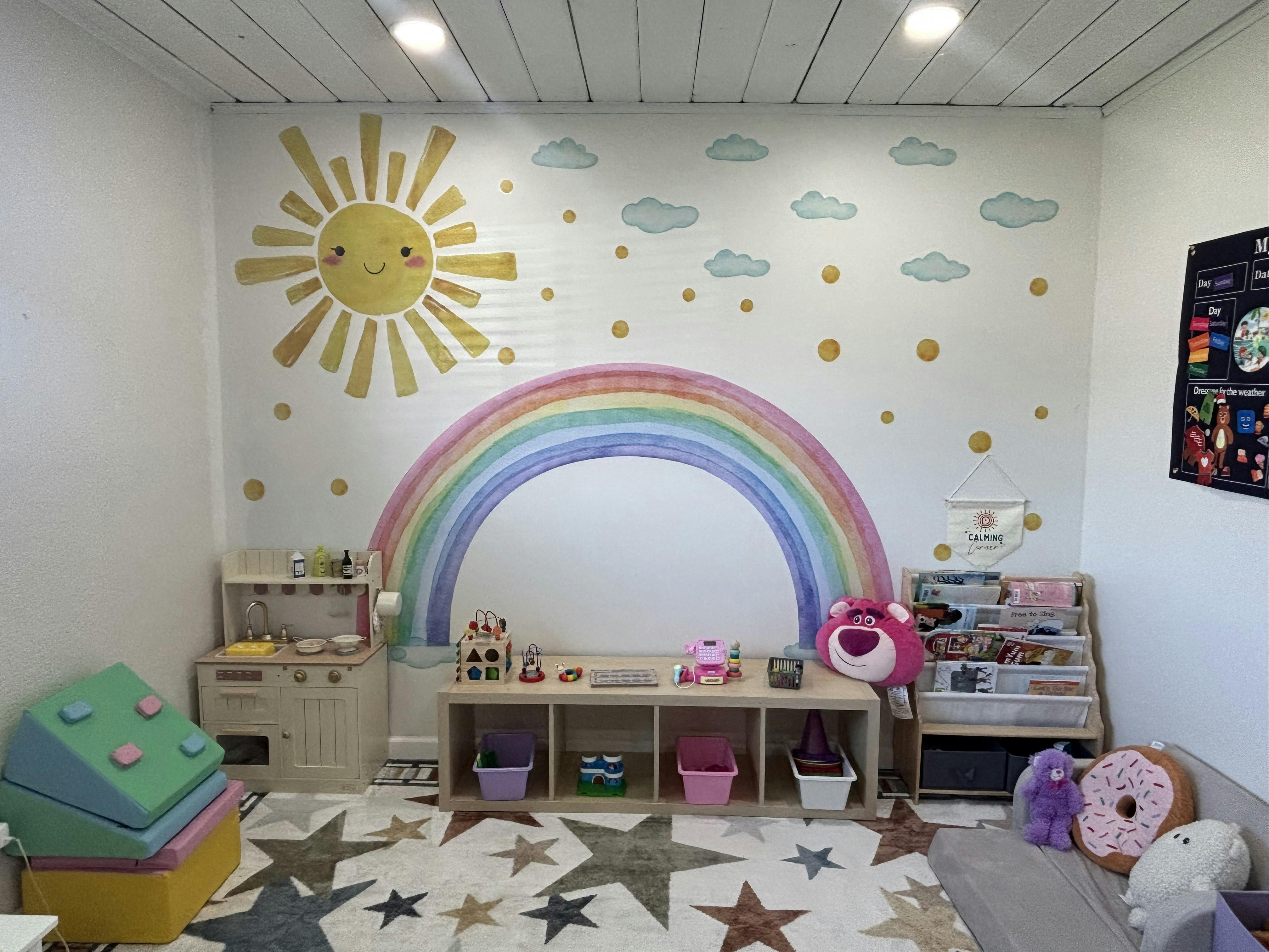 Playroom with sun and rainbow wall decals, play kitchen, and toys