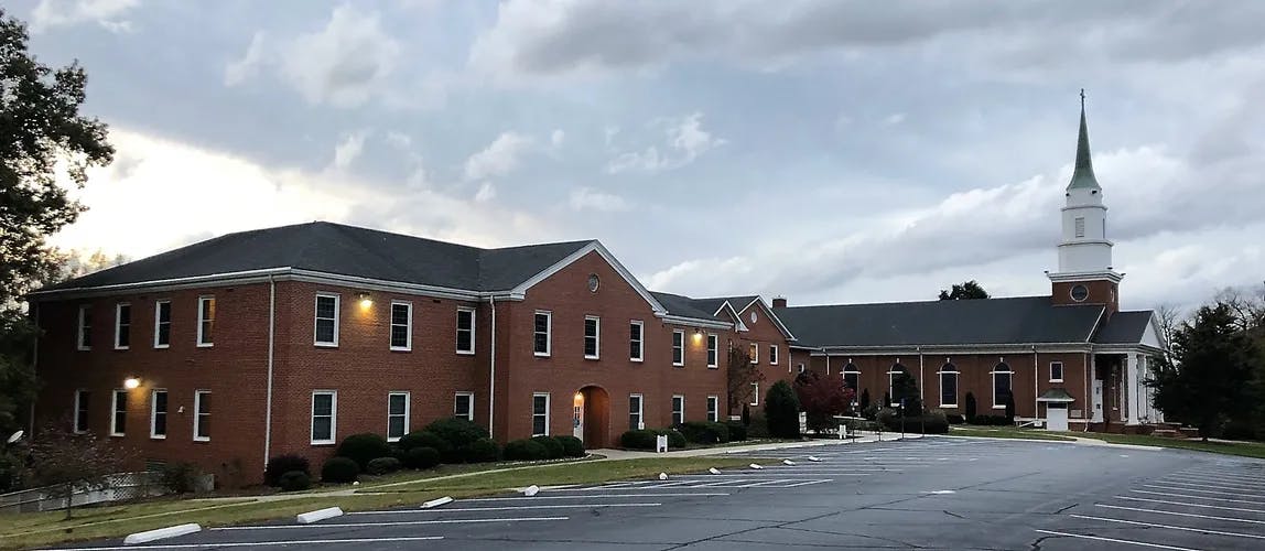 Brick building with a white steeple and a parking lot in front