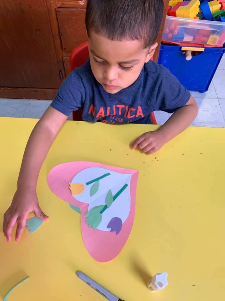 Child making a heart-shaped craft with paper flowers