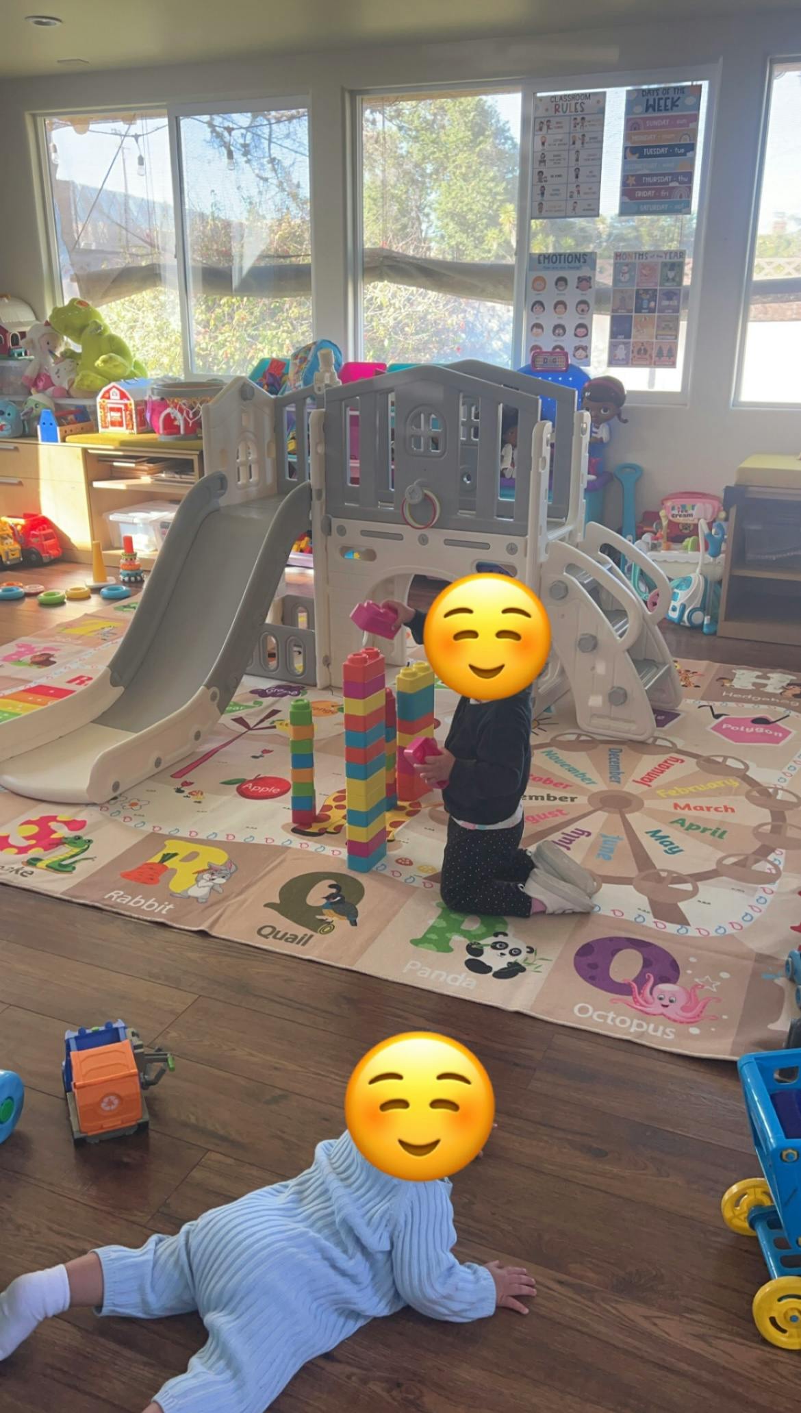 two children playing on a soft mat with toys in a bright room