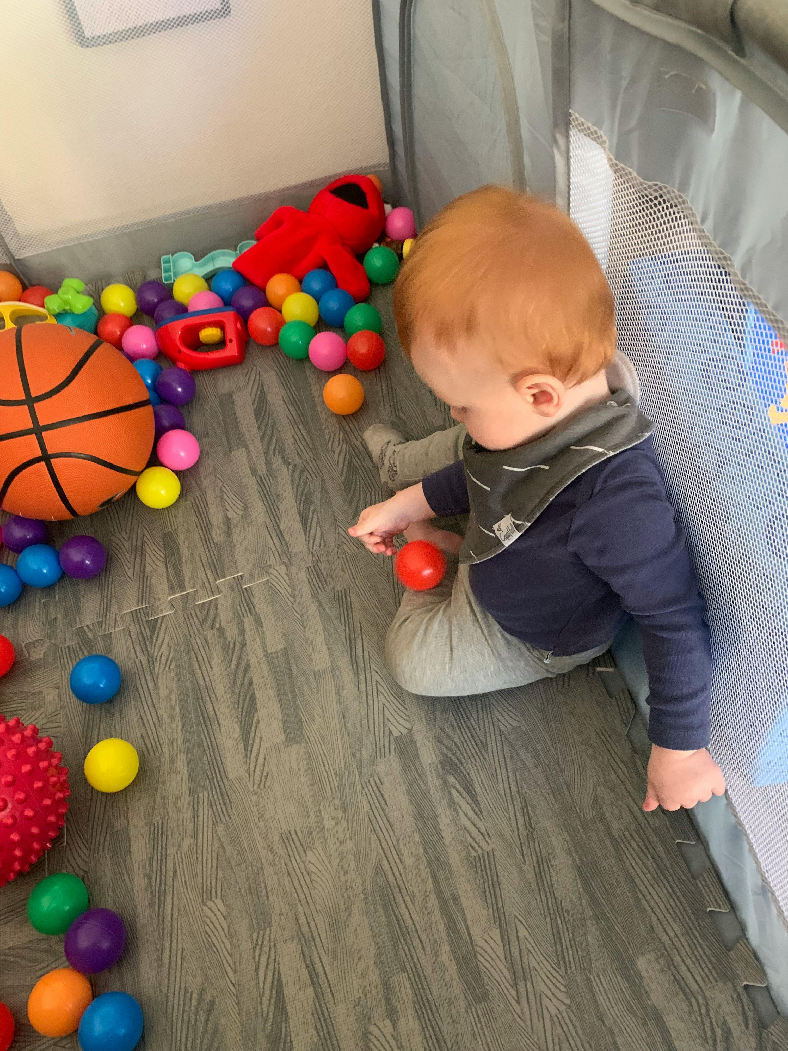 Child playing with a red ball among other toys