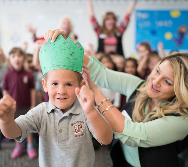 Adult placing a green paper crown on a child in a classroom