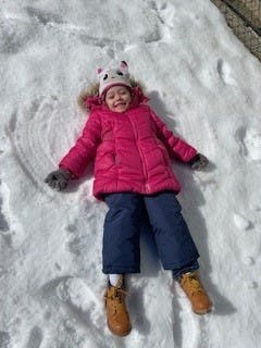 Child in winter coat and hat lying in snow making a snow angel