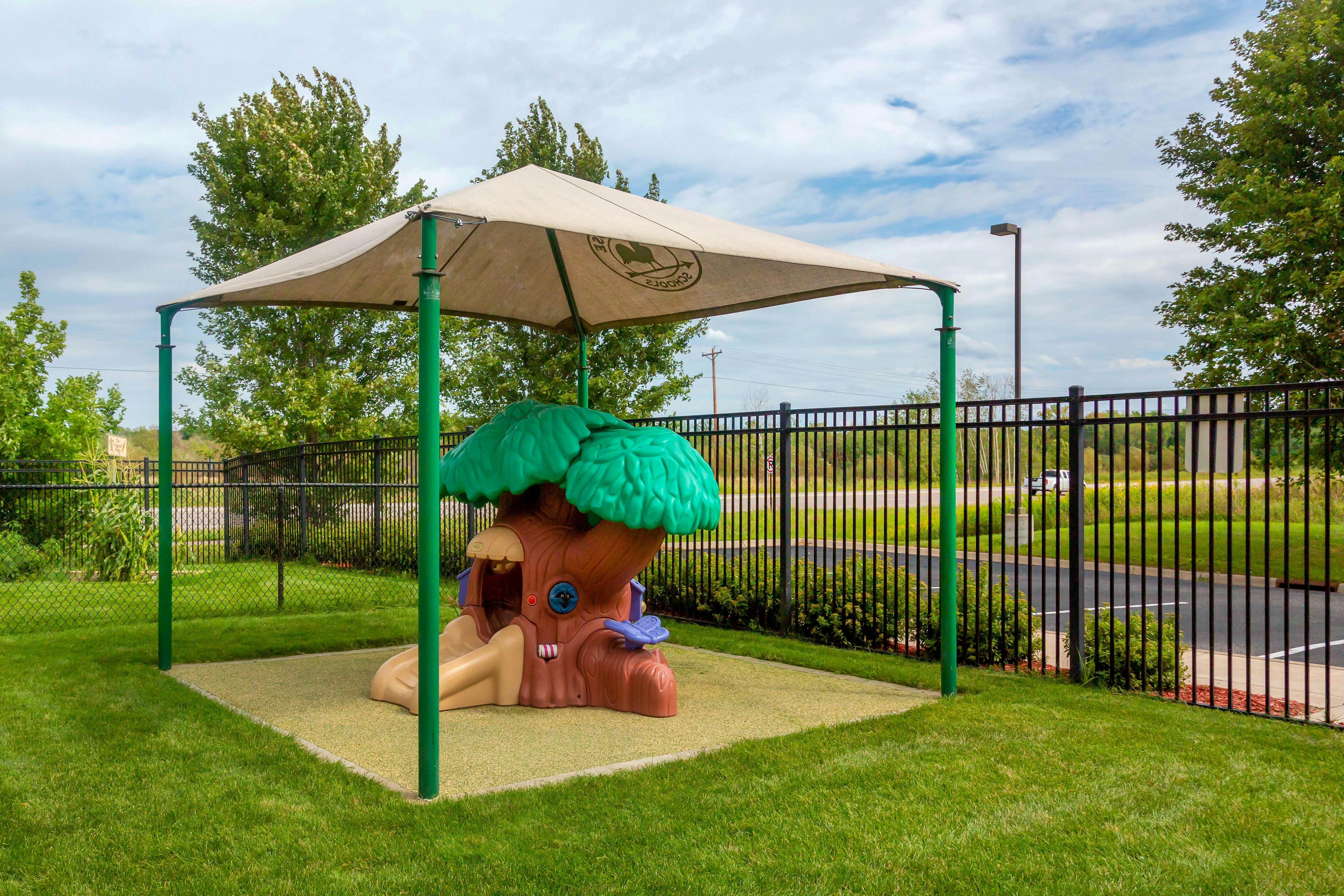 Playground area with a treehouse play structure under a canopy