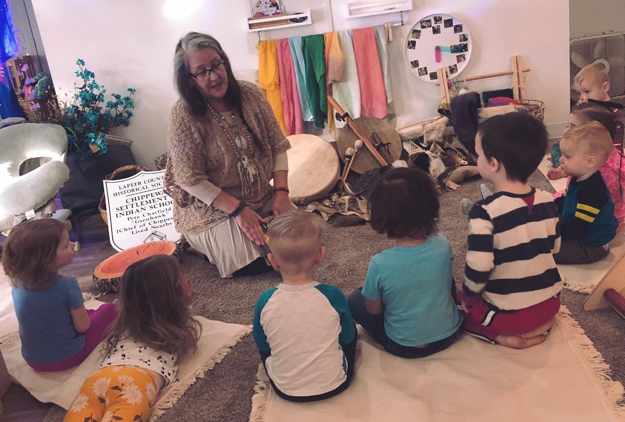 Person kneeling and speaking to a group of children sitting on the floor