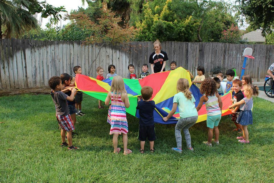 Children and an adult playing with a colorful parachute on a grassy lawn