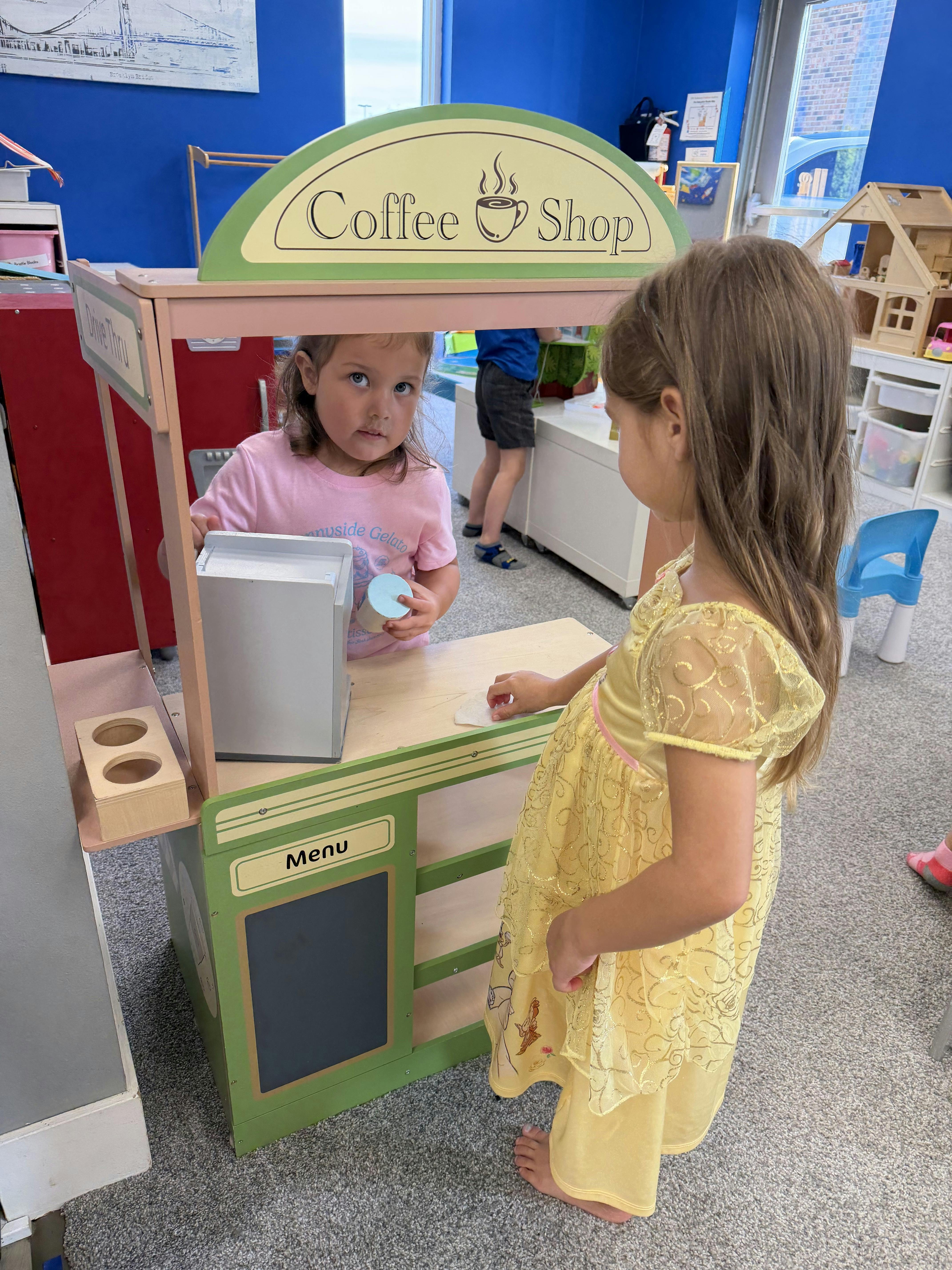 Two children playing with a toy coffee shop stand
