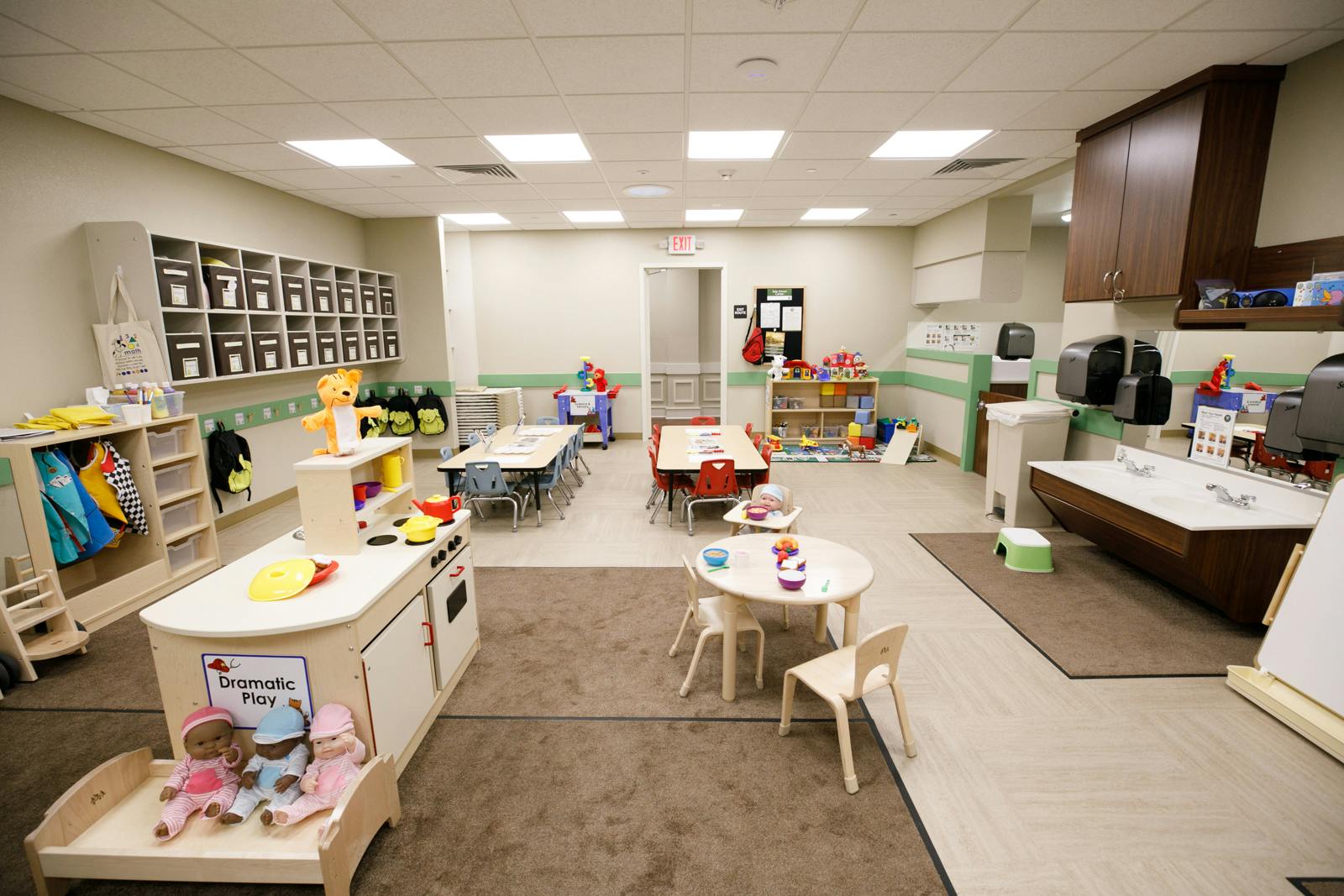 Empty classroom with small tables and chairs, play kitchen, and shelves