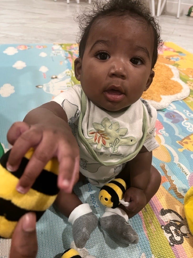 Child sitting on a play mat reaching for a small bee toy