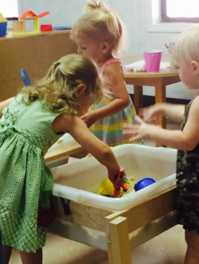 Three children playing with toys in a water table