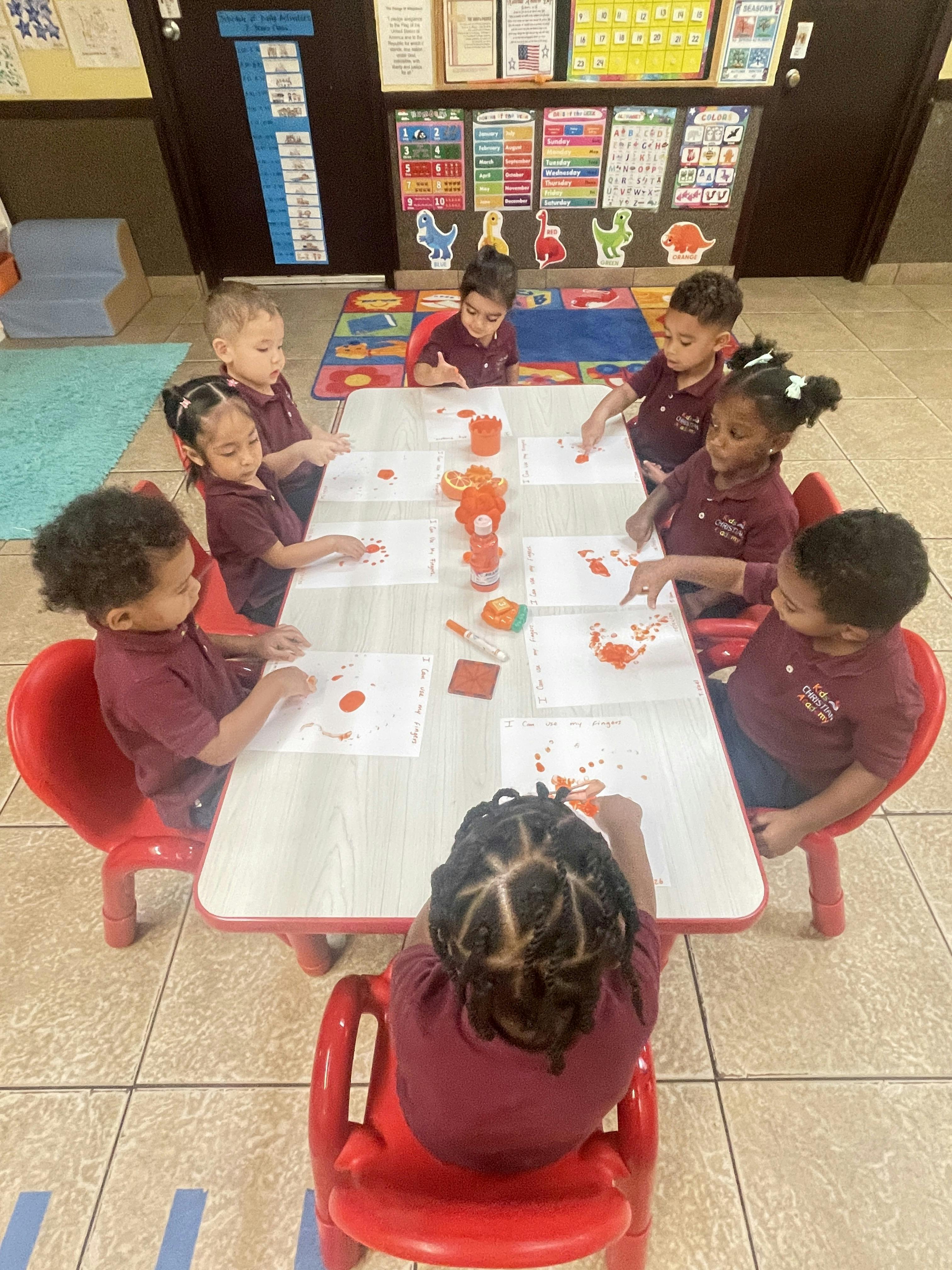 Group of children doing finger painting at a table in a classroom