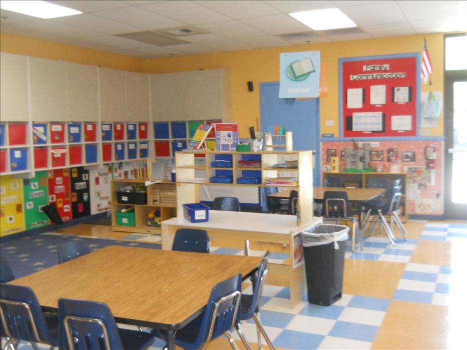 An empty classroom with multiple tables, chairs, and learning materials