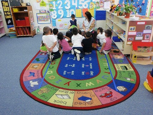 Adults and children sitting on a colorful rug in a classroom