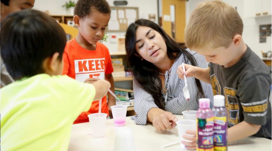 Adult and three children mixing liquids in cups in a classroom
